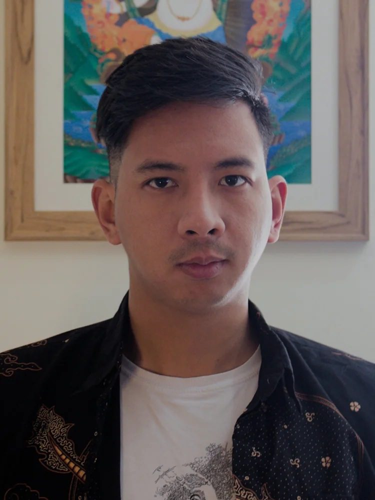 Man posing indoors, colorful artwork behind.