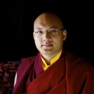 Monk wearing glasses in dark background.