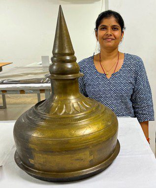 A woman standing behind a large, ornate brass object.