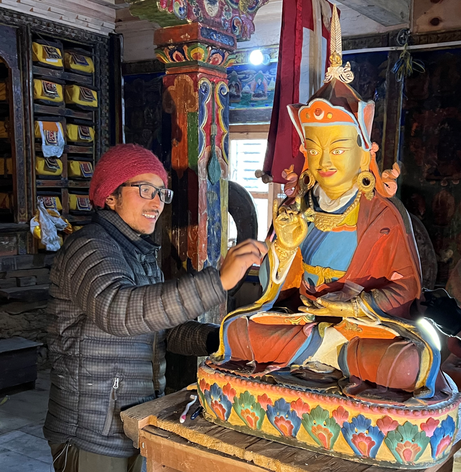 A man lighting incense in front of a colorful Buddha statue inside a temple.