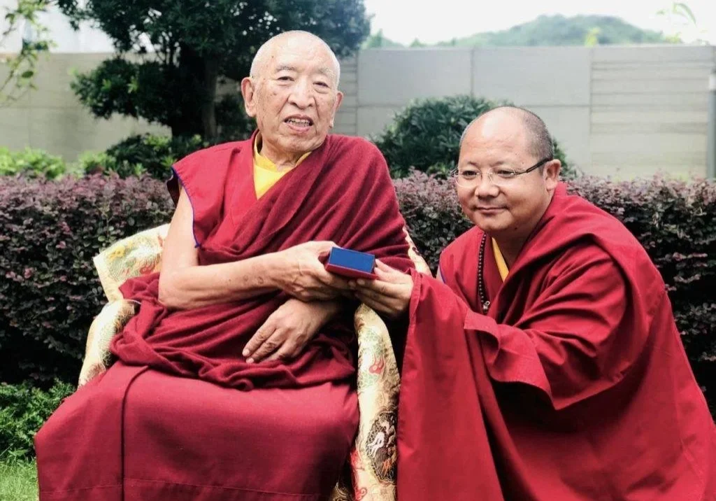 Two monks in red robes sitting outdoors.