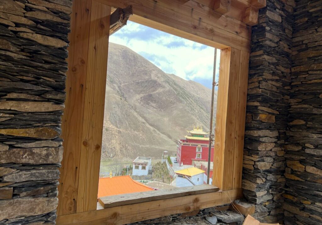 View of a mountain and colorful buildings through a rustic wooden window.