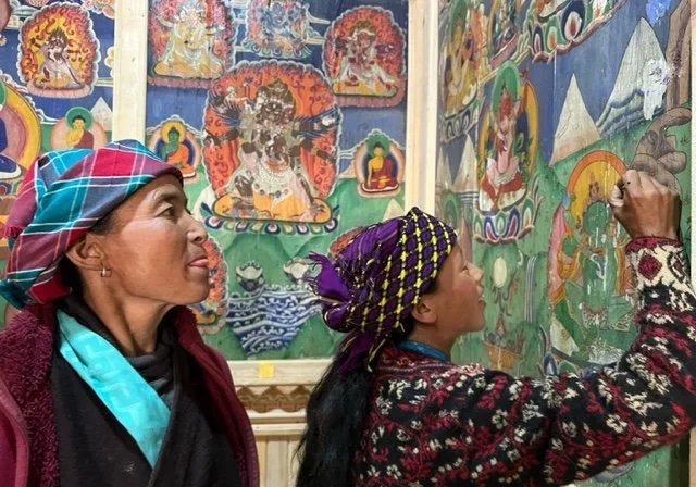 Women painting colorful traditional murals inside building.